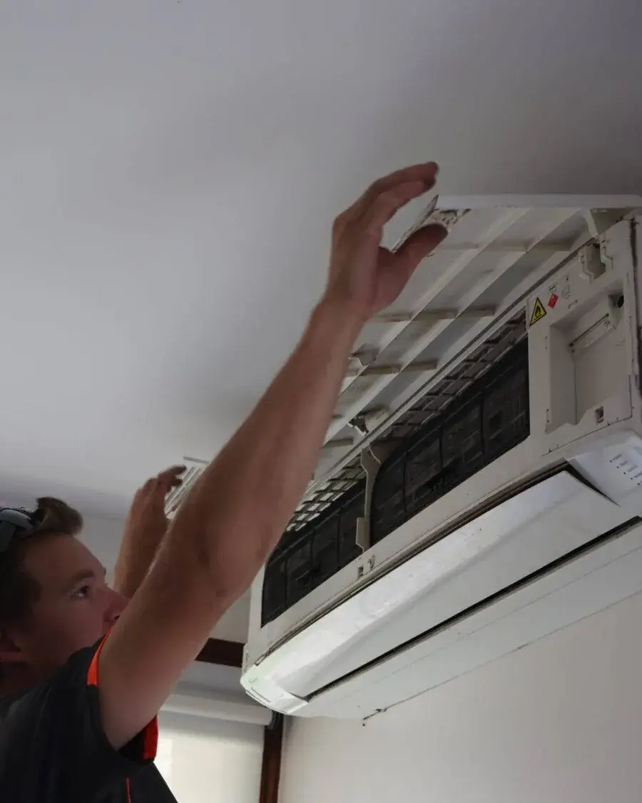 Technician performing maintenance on a wall-mounted air conditioning unit