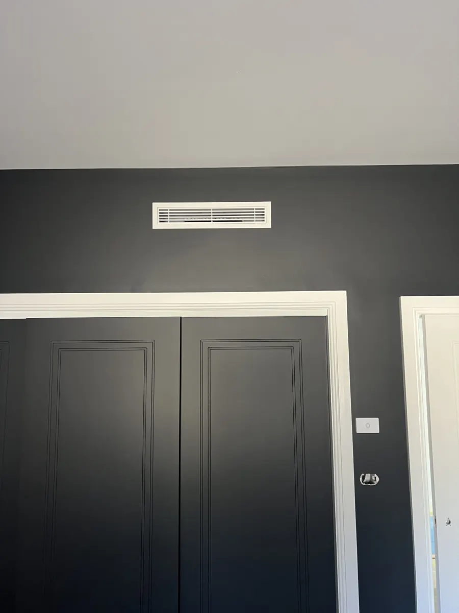 Ducted air conditioning bar grille mounted high on a dark feature wall above double doors