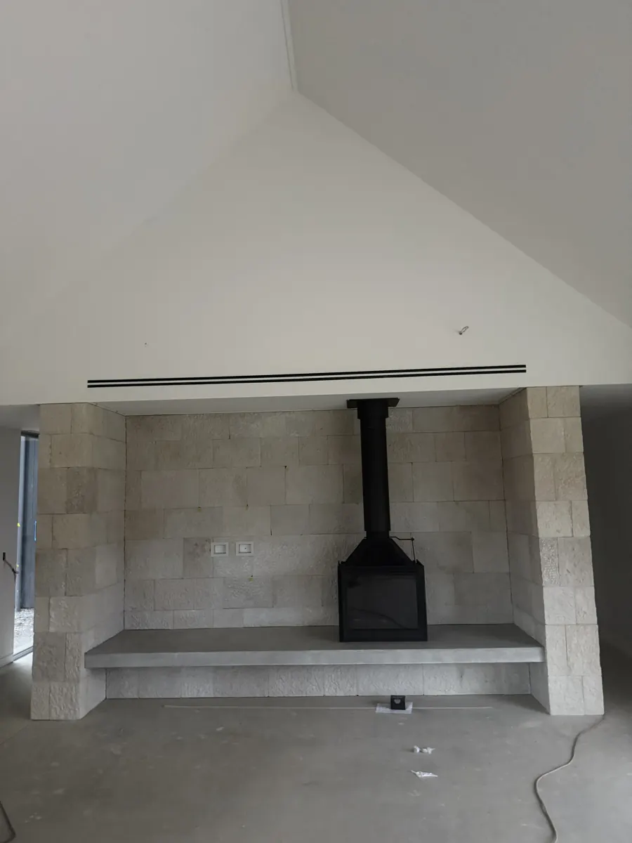 Slim linear slot ducted air conditioning diffuser above a fireplace under a raked ceiling