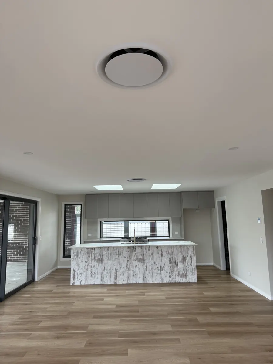 Round ducted air conditioning ceiling diffuser in an open-plan living and kitchen area