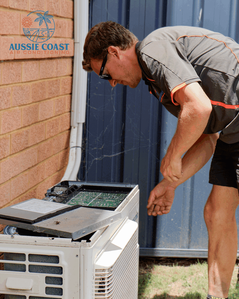 Technician servicing split system air conditioner, Aussie Coast Air logo visible, residential setting in Shoalhaven region.